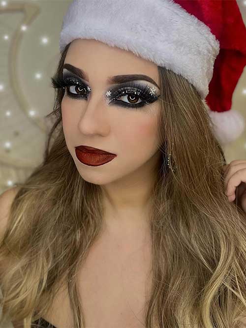 Black and silver eye look with small snowflakes, long lashes, and matte dark red lips. And wearing a Santa hat