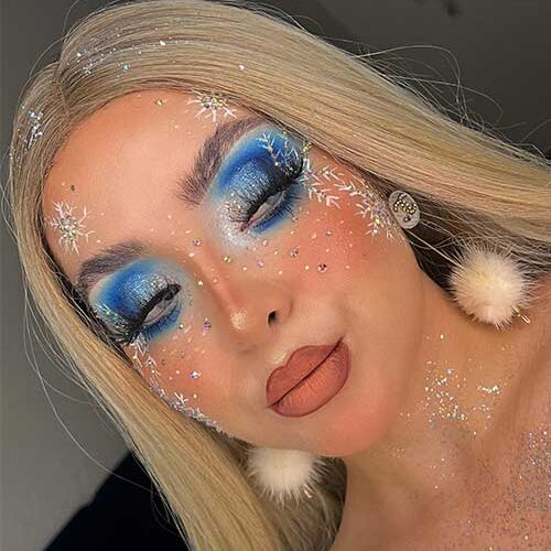 Blue Christmas eye makeup with silver glitter, matte nude lips, three big white snowflakes with silver glitter on the face