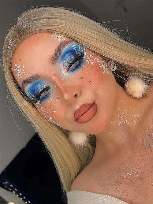 Blue Christmas makeup with silver glitter, matte nude lips, three big white snowflakes with silver glitter on the face