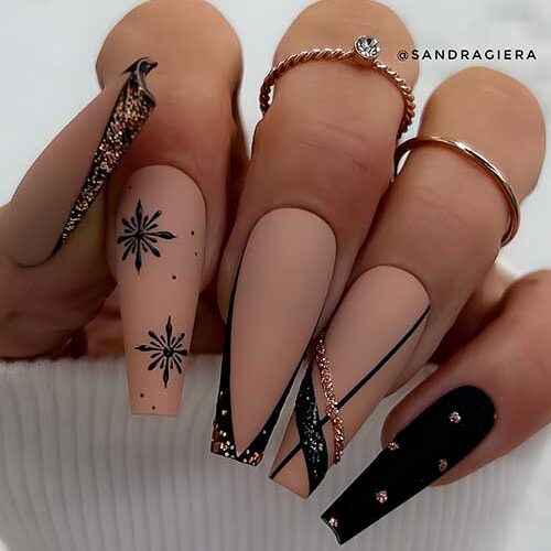 Classy matte nude nails with black design feature black snowflakes and two V-shaped black French tip nails with gold glitter