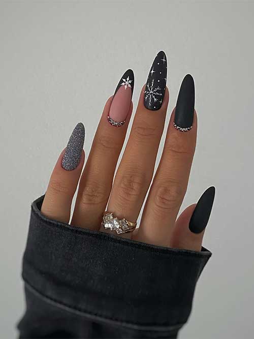 Matte black nails with white snowflakes, a silver glitter accent nail, and rhinestones on two accent black nails
