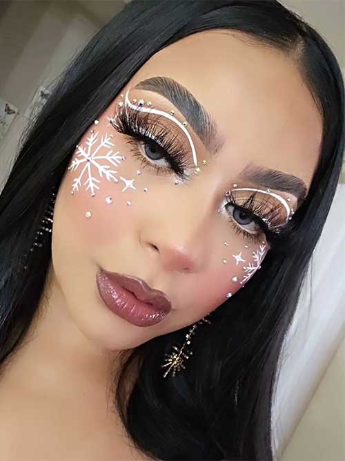 Nude Christmas makeup look with white graphical eyeliner, glossy nude lips, white snowflakes with sparkling rhinestones
