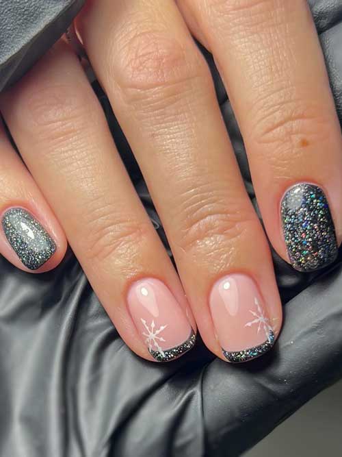 Short black nails with holographic glitter and two accent French tip nails adorned with a white snowflake on each nail