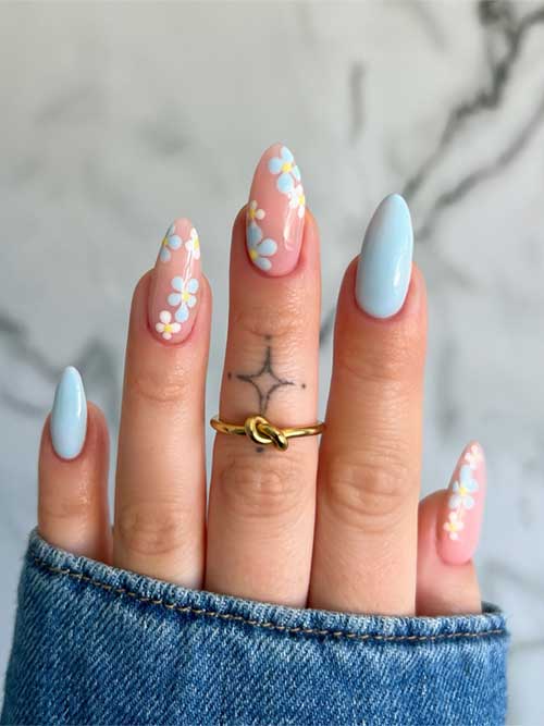 Elegant light blue nails adorned with daisy designs, featuring almond shape and a stylish gold knot ring for added flair. Elegant light blue nails adorned with daisy designs, featuring almond shape and a stylish gold knot ring for added flair.