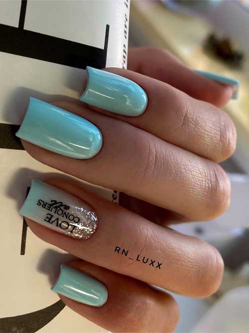 Light blue nails with a glossy finish, featuring a glittery ring finger with "LOVE CONQUERS ALL" and stylish silver rings. Light blue nails with a glossy finish, featuring a glittery ring finger with "LOVE CONQUERS ALL" and stylish silver rings.