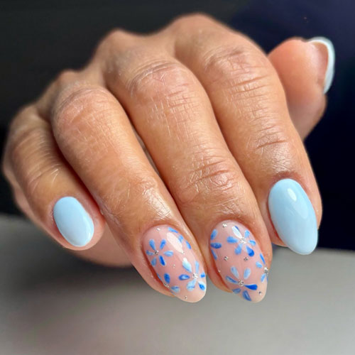 Light blue nails with floral accents feature daisy designs on nude pink, creating a dreamy, nature-inspired look.