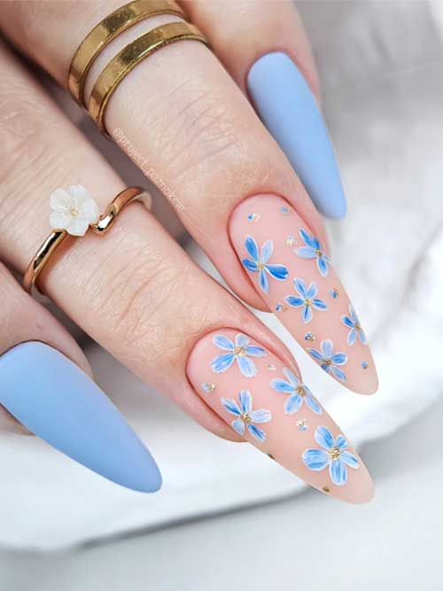 Matte light blue nails with nude pink accents feature delicate daisy designs and gold glitter dots for a whimsical floral look. Matte light blue nails with nude pink accents feature delicate daisy designs and gold glitter dots for a whimsical floral look.