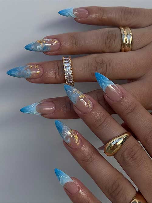 Almond-shaped ocean nails feature a blue-to-white ombré with gold foil accents, evoking sea foam and summer elegance. Almond-shaped ocean nails feature a blue-to-white ombré with gold foil accents, evoking sea foam and summer elegance.